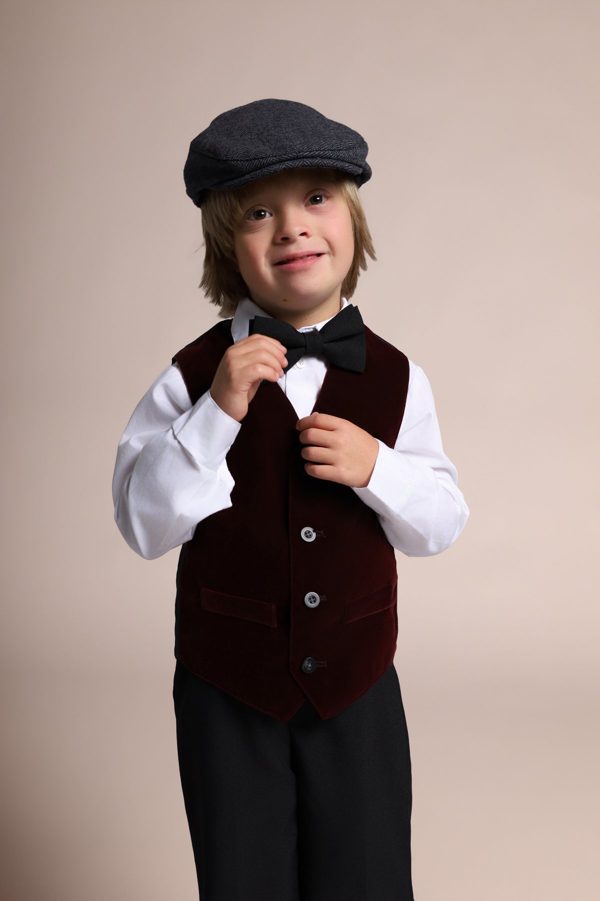 Wesley Wyatt in a newsboy cap adjusting his bow tie, smiling
