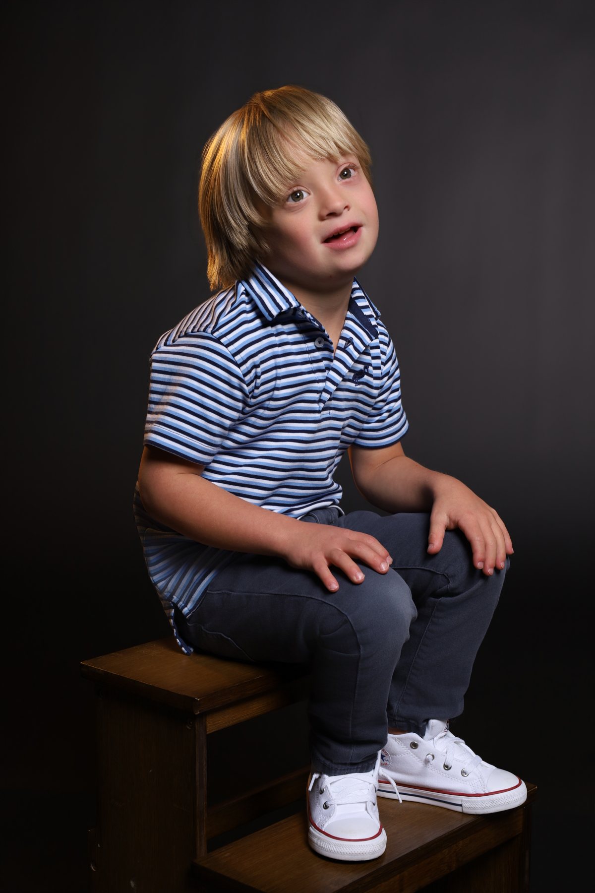 Wesley Wyatt seated on a wooden crate in a striped polo, looking up
