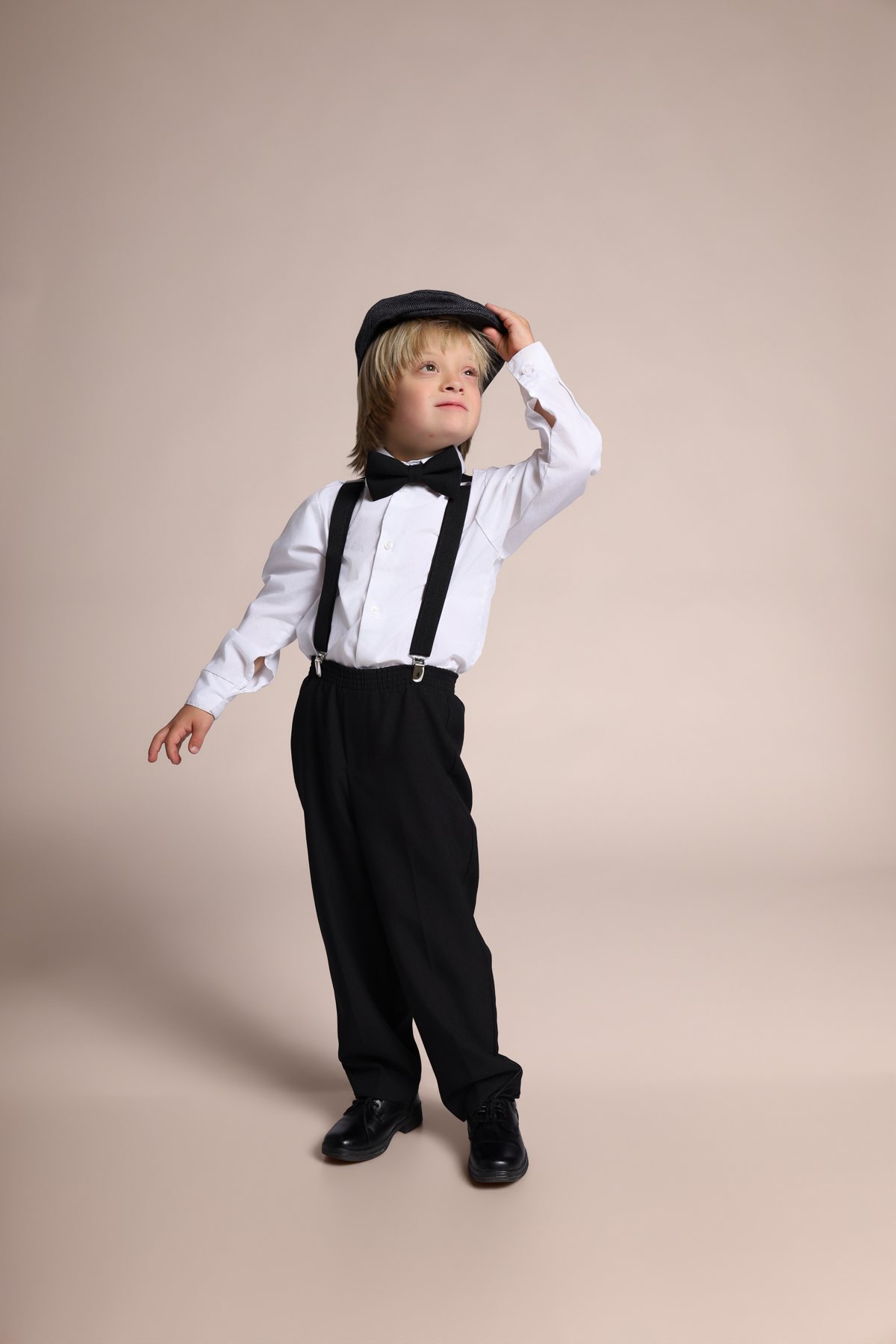 Wesley Wyatt tipping his newsboy cap, full-length in suspenders and bow tie