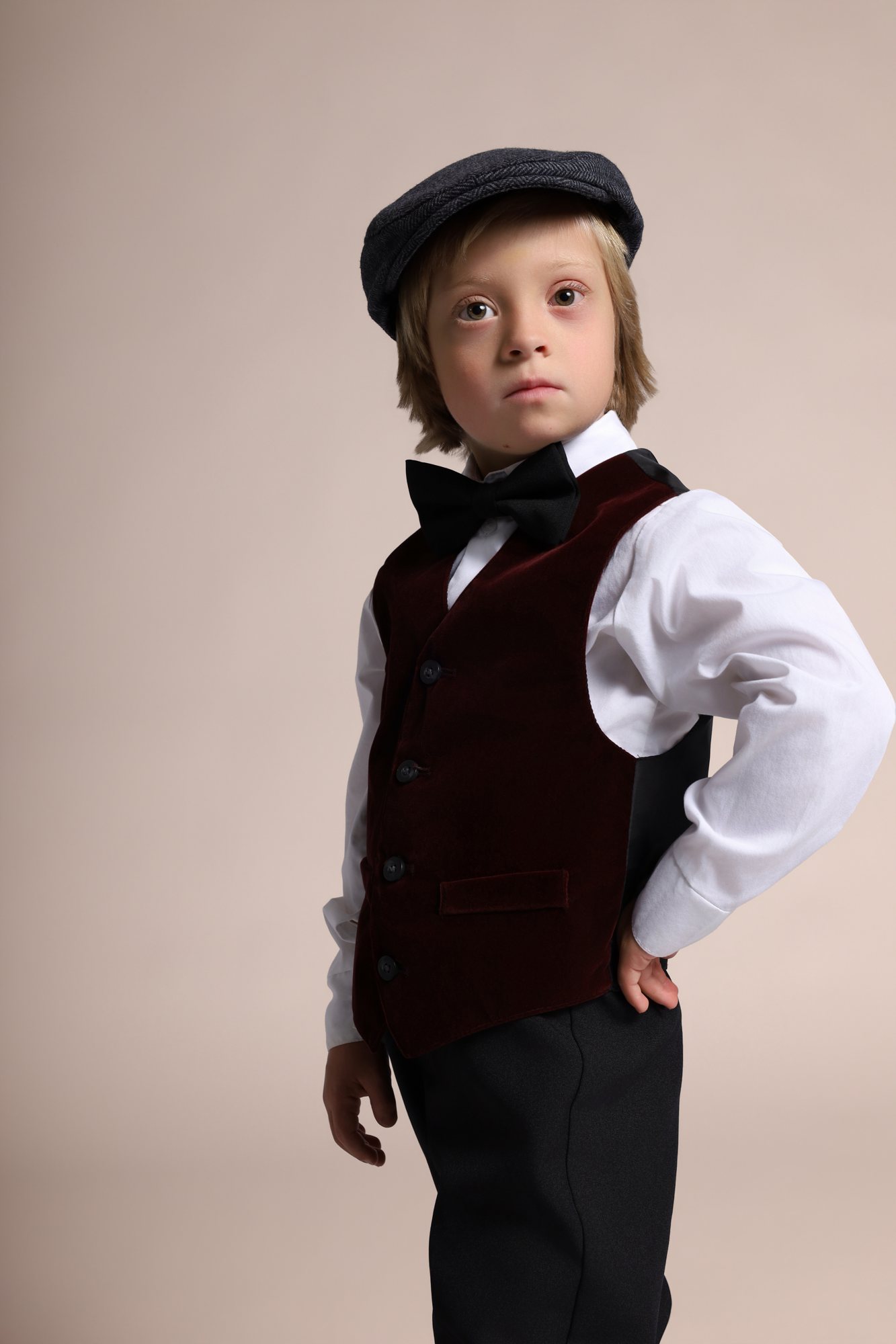 Wesley Wyatt in a newsboy cap, velvet vest, and bow tie, hand on hip